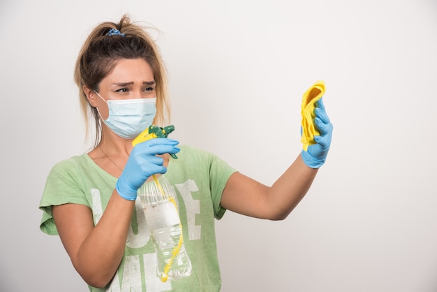Personne masquee nettoyant des moisissures sur un mur blanc avec un chiffon et un spray